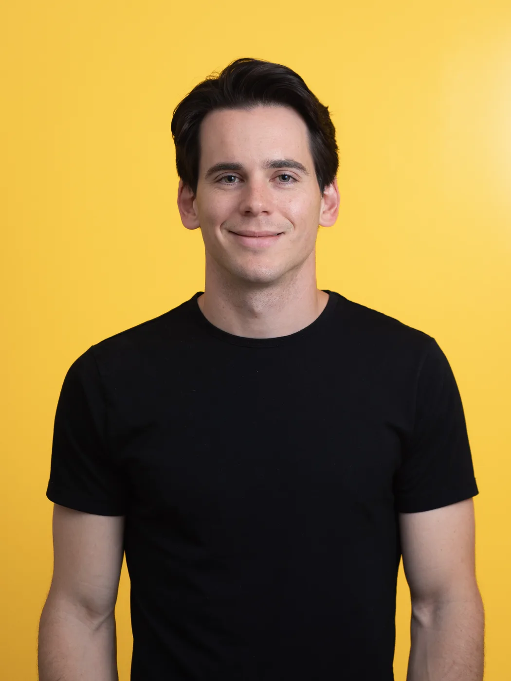 John Goddard, smiling, in a black T-shirt against a yellow backdrop