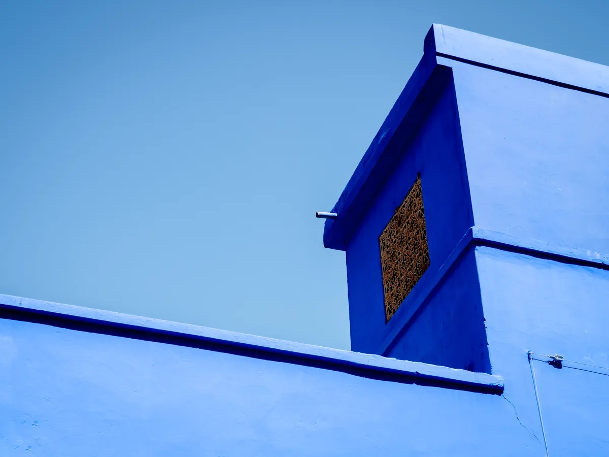 A cobalt-blue wall and window against a pale sky