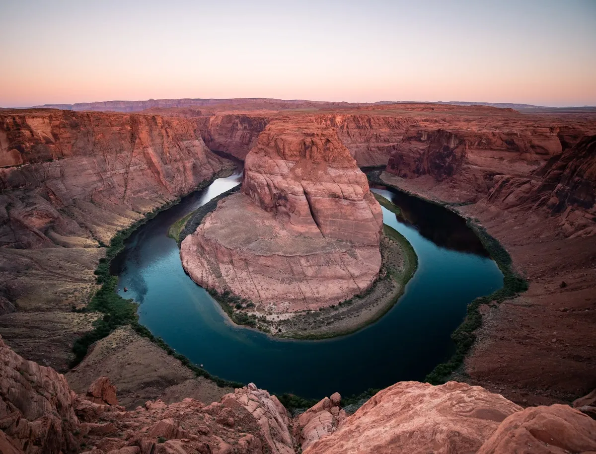A river curving in a tight horseshoe around a red sandstone butte at dusk