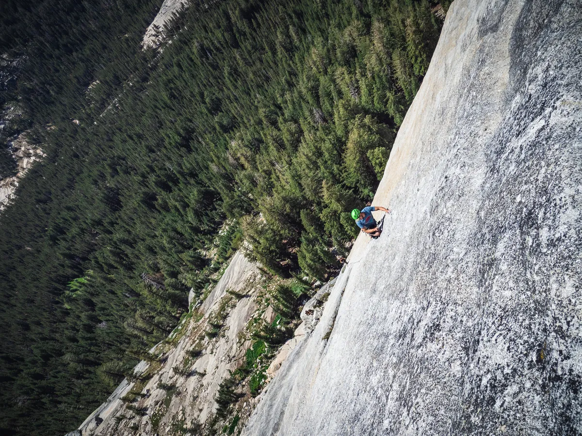 Looking down a vast granite slab to a small climber and the forest far below